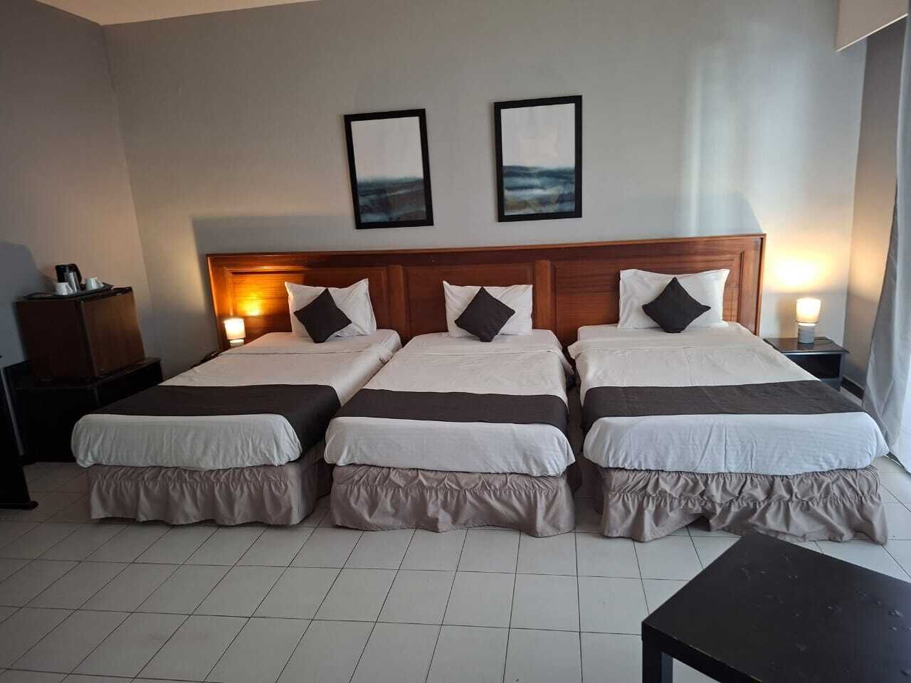 Quarto de hotel com três camas, uma mesa de cabeceira e duas fotos emolduradas na parede.