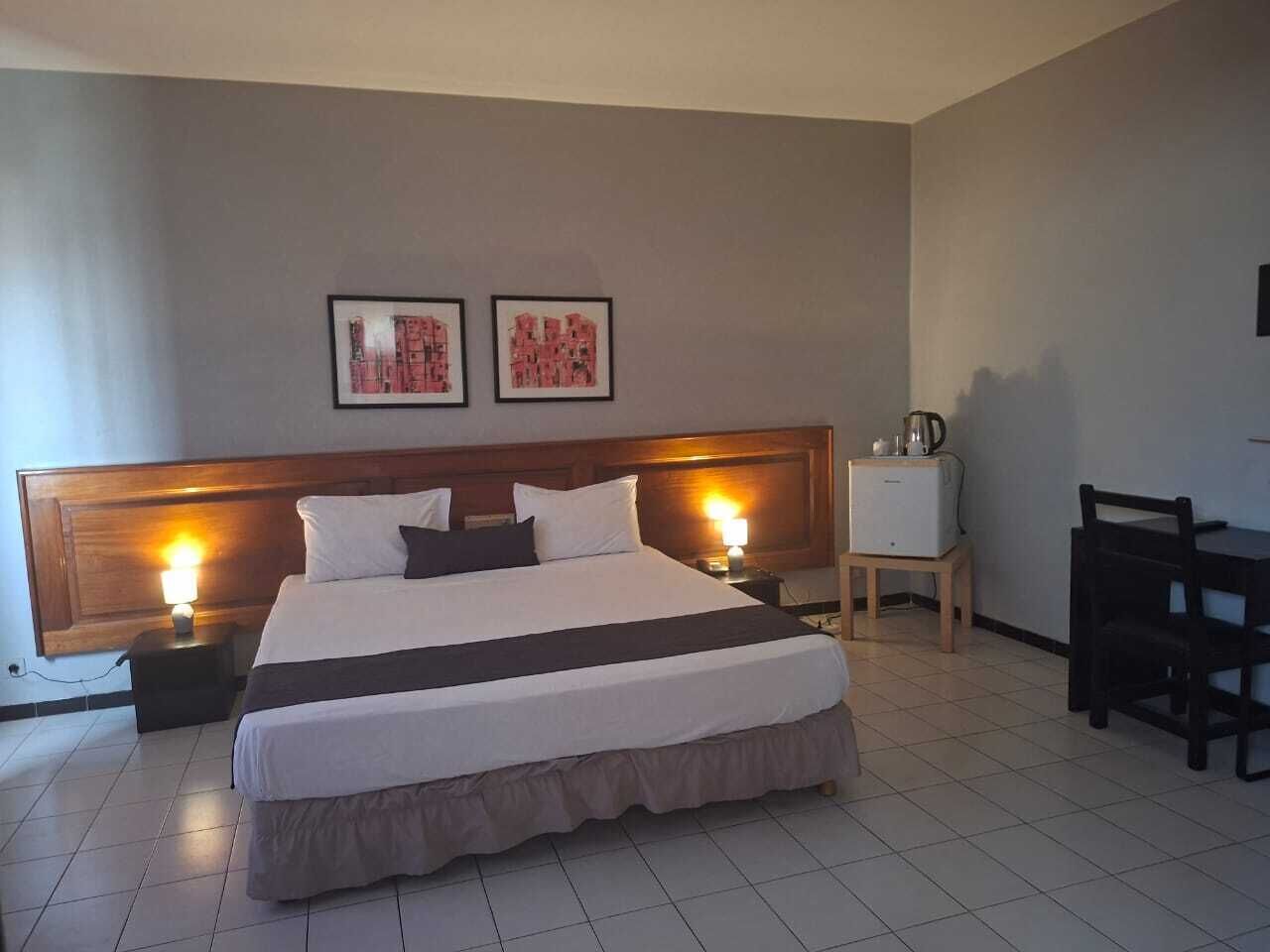 A hotel room with a large bed, bedside tables, a desk, and two framed pictures on the wall.