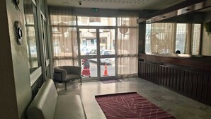 A hotel lobby with a sofa, a red patterned rug, and a view of the street through large windows. - hotel BARAKA (Dakar)