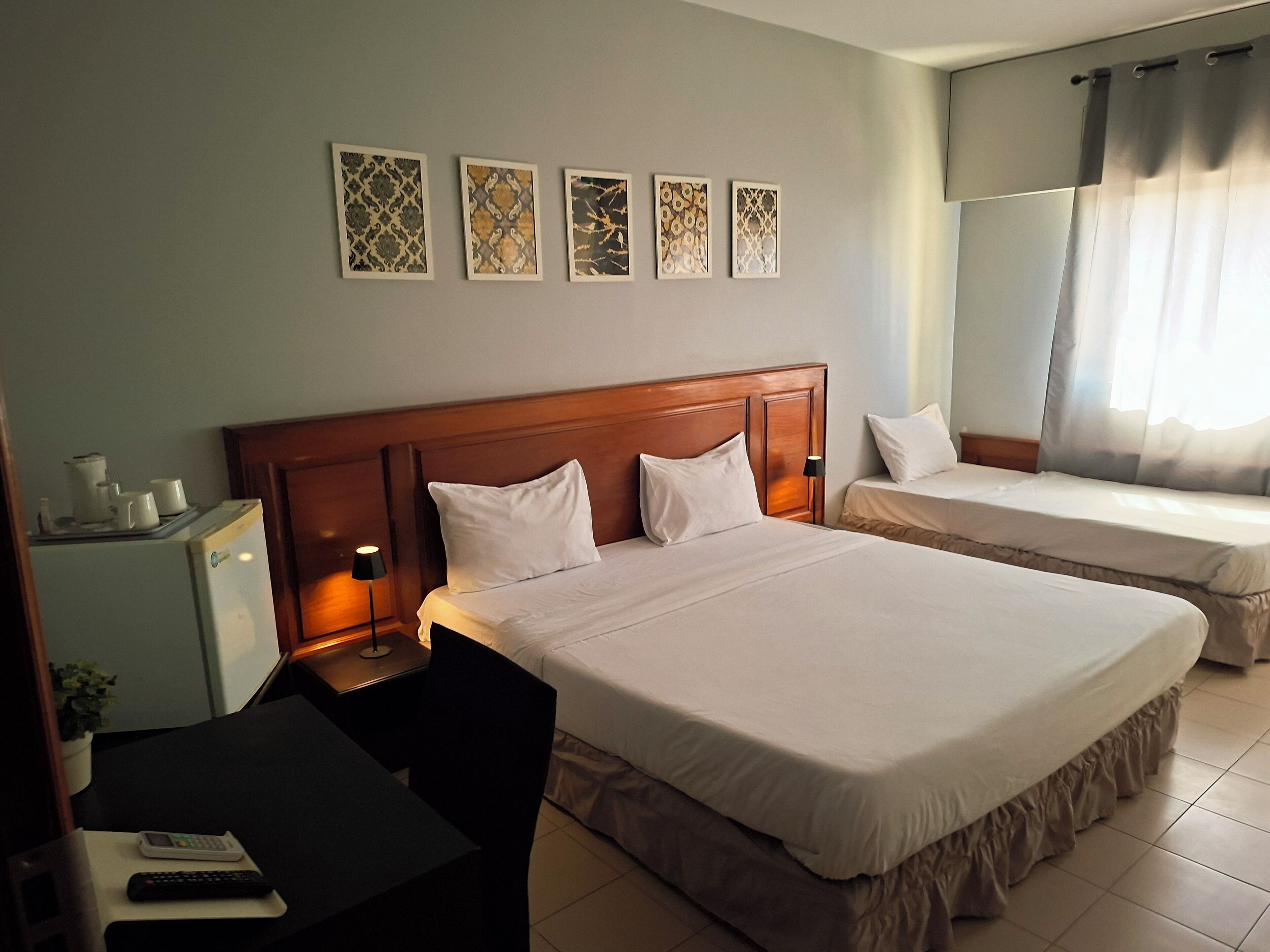 Une chambre d’hôtel avec deux lits, un bureau avec une chaise, un petit réfrigérateur et une lampe fixée au mur.