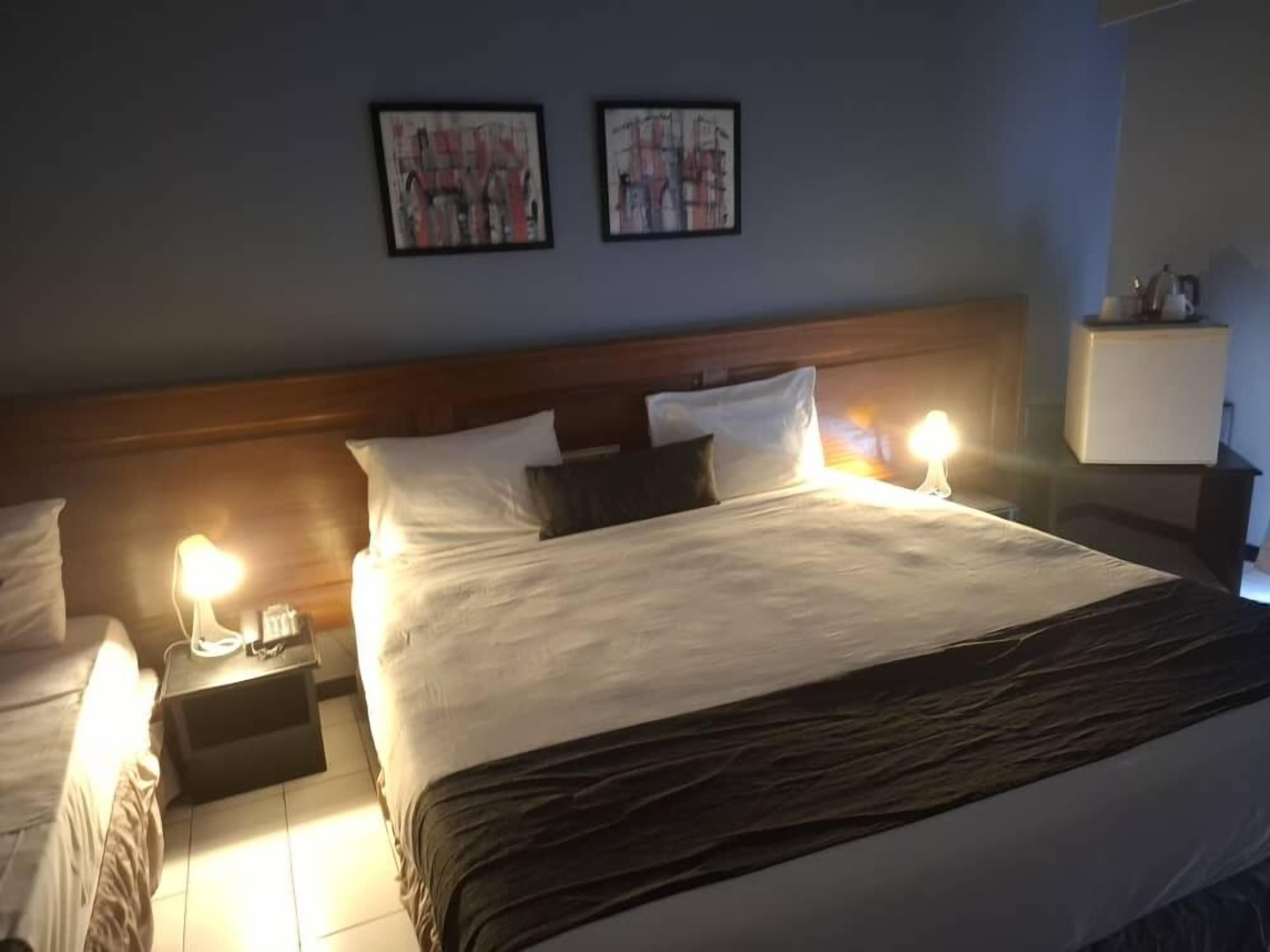 A hotel room with a large bed, two bedside tables with lamps, and two framed artworks on the wall.