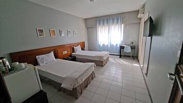 Une chambre d’hôtel avec deux lits, un bureau, une chaise, un réfrigérateur et une fenêtre avec des rideaux.