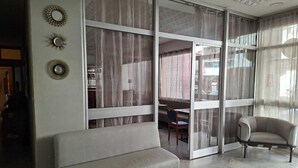 A living room with a sofa, armchair, and large windows with curtains. - hotel BARAKA (Dakar)