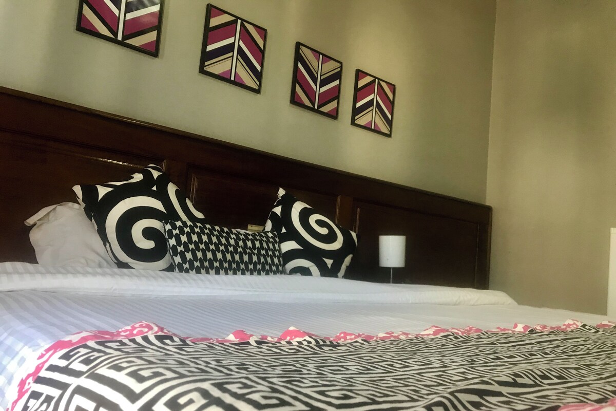 Una camera d'albergo con un letto, cuscini decorati e tre opere d'arte appese al muro.