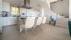 Eine moderne Küche mit weißen Schränken, einer Edelstahl-Dunstabzugshaube und einem Essbereich mit weißen Stühlen.