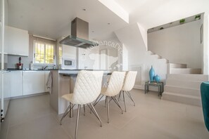 A modern kitchen with white cabinets, a stainless steel range hood, and a dining area with white chairs. - CostaBlancaDreams - Didi in Altea (Altea)