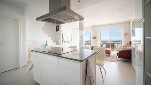Eine moderne Küche mit Kochinsel, ein Essbereich mit Tisch und Stühlen sowie ein Wohnzimmer mit Sofa und Blick ins Freie.