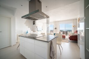 A modern kitchen with a central island, a dining area with a table and chairs, and a living room with a sofa and a view of the outdoors. - CostaBlancaDreams - Didi in Altea (Altea)