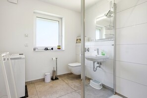 A modern bathroom with a toilet, a sink, a shower, and a window. - Family & friends - Holiday apartment family & friends: balcony, elevator & great (Norden)