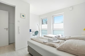 A modern bedroom with a bed, a desk, and a chair. - Family & friends - Holiday apartment family & friends: balcony, elevator & great (Norden)