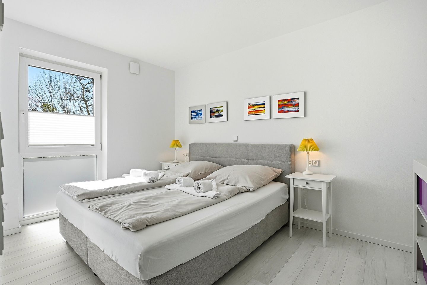 A modern bedroom with a bed, two bedside tables, a window, and wall art.