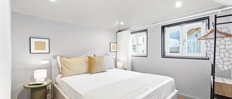 A modern hotel room with a large bed, bedside tables, a wardrobe, and a window with a view of buildings.