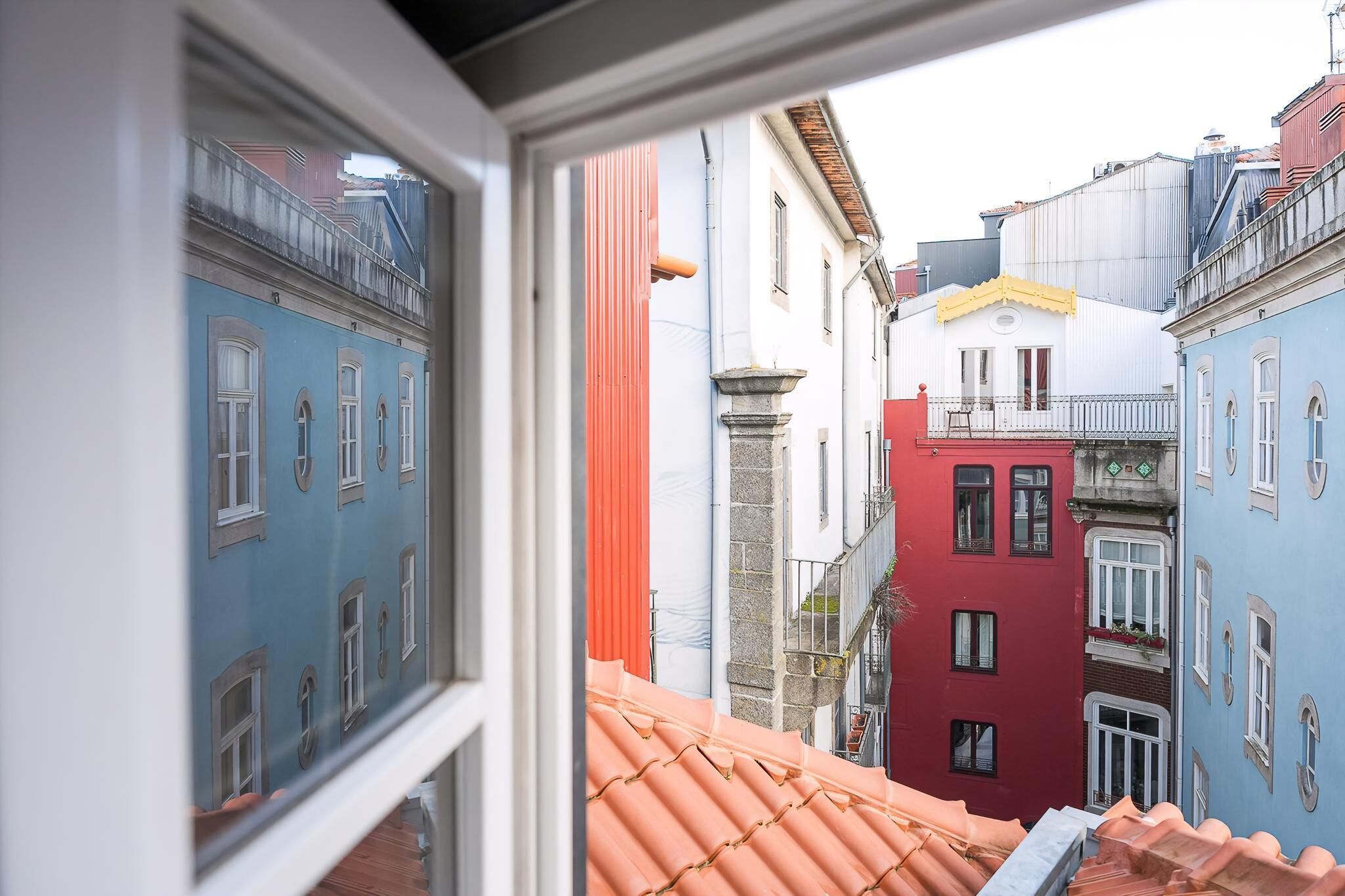 A narrow street with colorful buildings, a visible window, and a red-tiled roof.