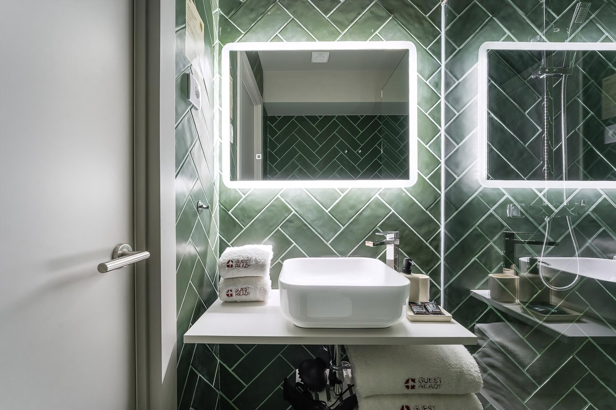 A bathroom with a white sink, a mirror, and a shower. There are towels and toiletries on the counter.