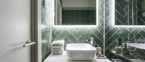 A bathroom with a white sink, a mirror, and a shower. There are towels and toiletries on the counter.