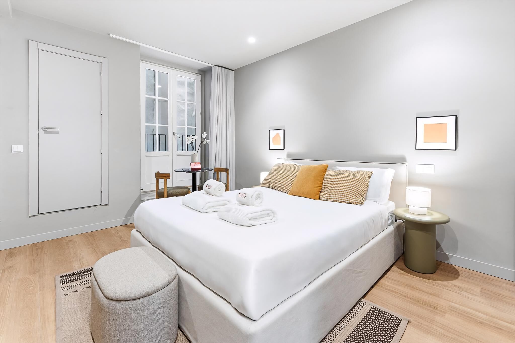 A modern hotel room with a bed, bedside table, lamp, and a window with curtains.
