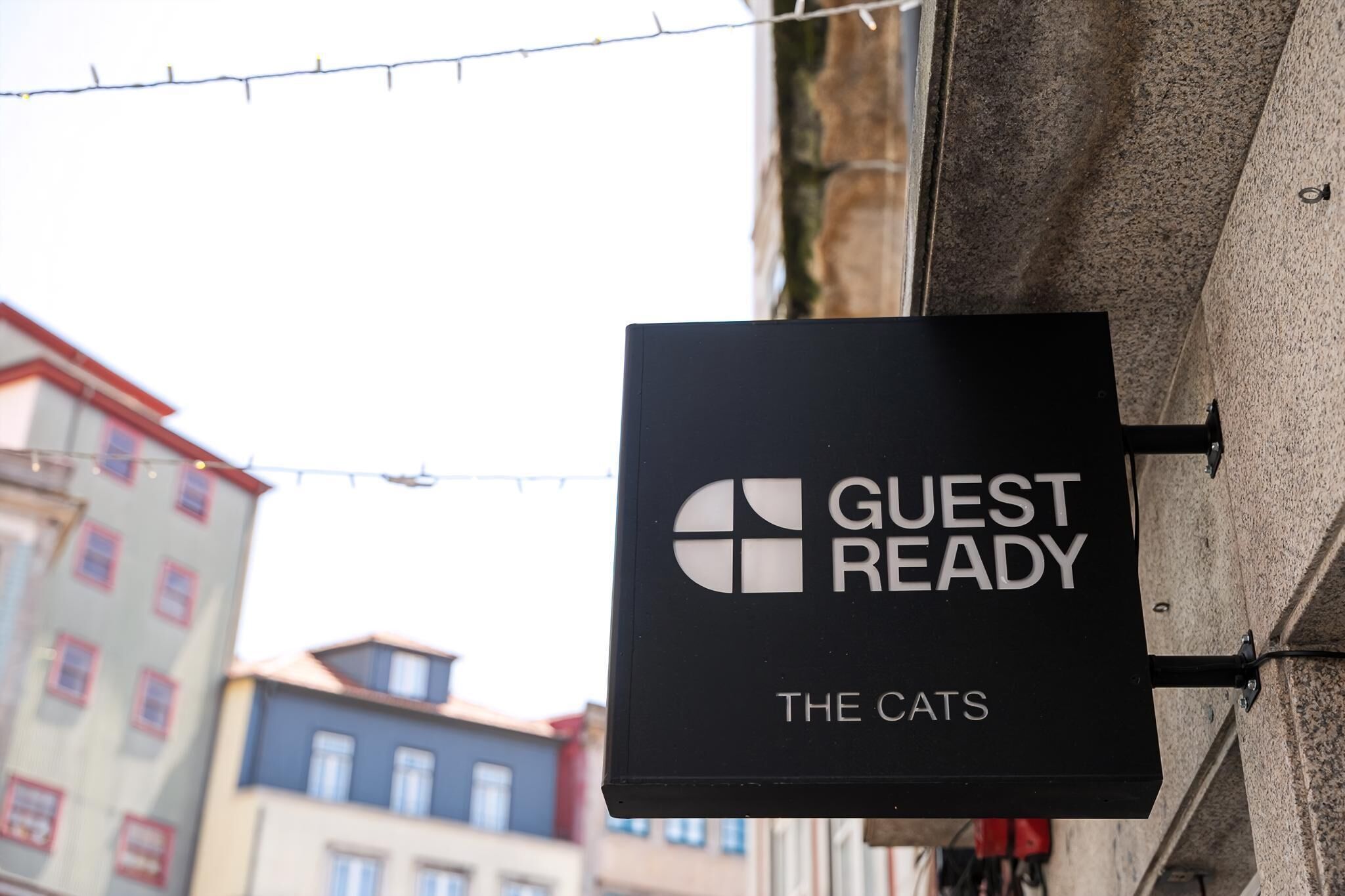 Et sort skilt med teksten 'GUEST READY' og 'THE CATS' på en bygningsfacade.