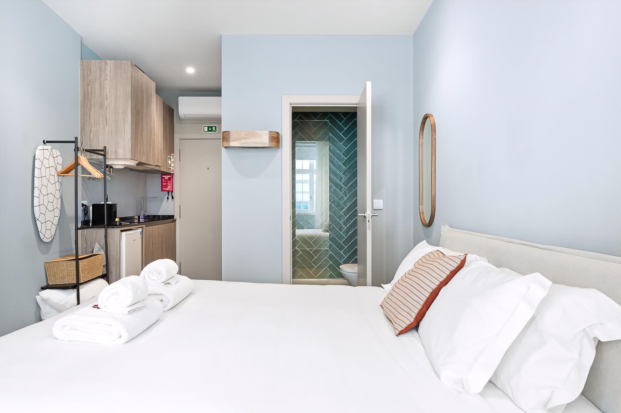 A hotel room with a bed, a bathroom with a herringbone tile wall, a kitchenette, and a hanging towel rack.