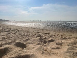 Een zandstrand met voetafdrukken, een heldere lucht en mensen in de verte.