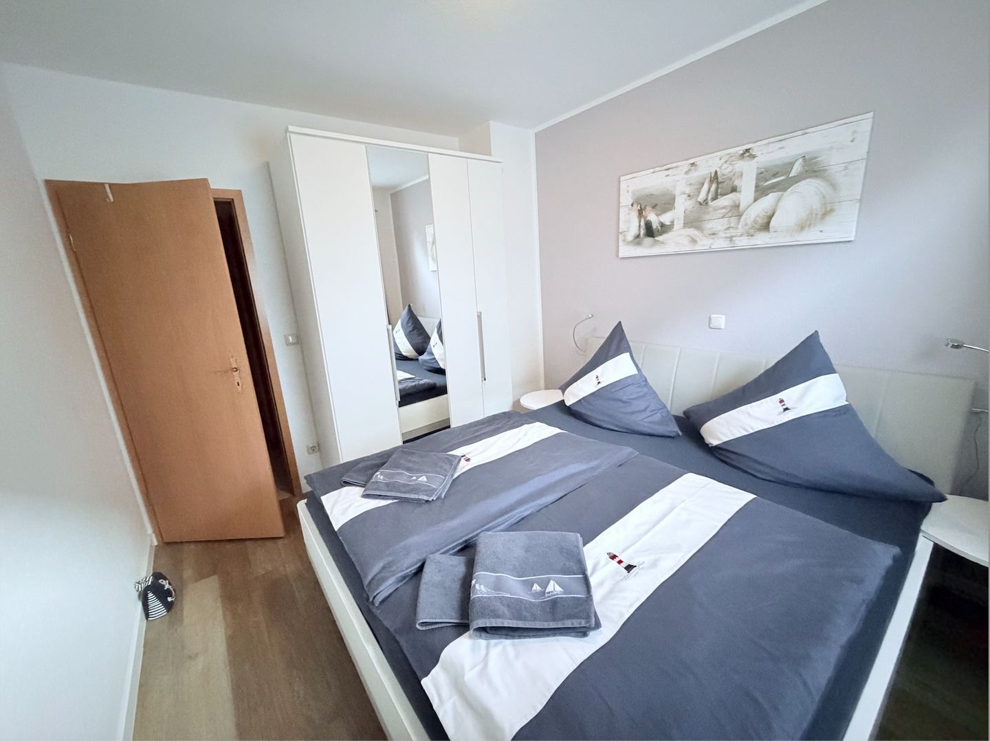Un dormitorio con cama, una puerta, un espejo y una obra de arte colgada en la pared.