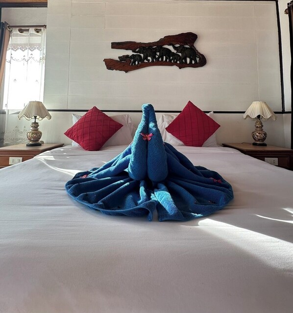 A neatly made bed with a blue towel arranged in a fan shape, two red pillows, and a wooden wall art piece above the bed. - beachfront villa (Ko Chang)