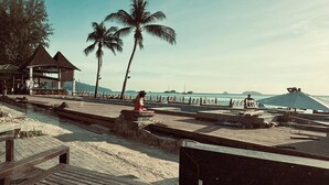 A beachside area with wooden benches, a palm tree, and a small pavilion. - beachfront villa (Ko Chang)