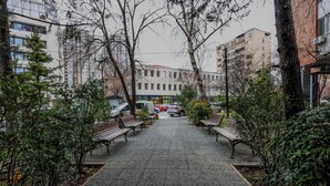 A paved walkway with benches, surrounded by trees and buildings. - Urban Zen  Skopje Modern 1BR in Skopje Center ,Quiet & Fully Equipped (Skopje)