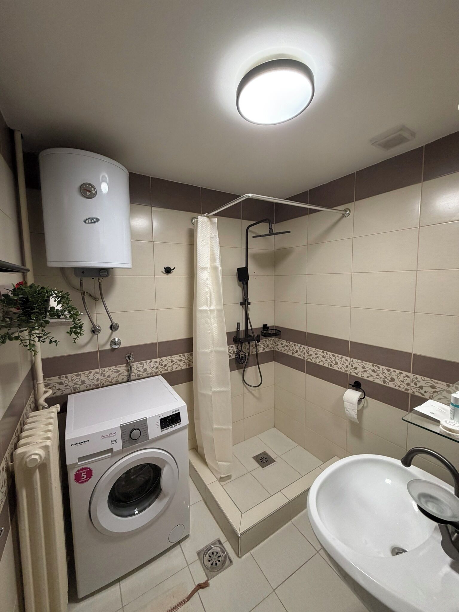 A compact bathroom with a washing machine, a shower, and a sink.