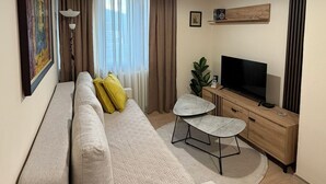 A modern living room with a sofa, a small round table, a TV, and a plant. - Urban Zen  Skopje Modern 1BR in Skopje Center ,Quiet & Fully Equipped (Skopje)