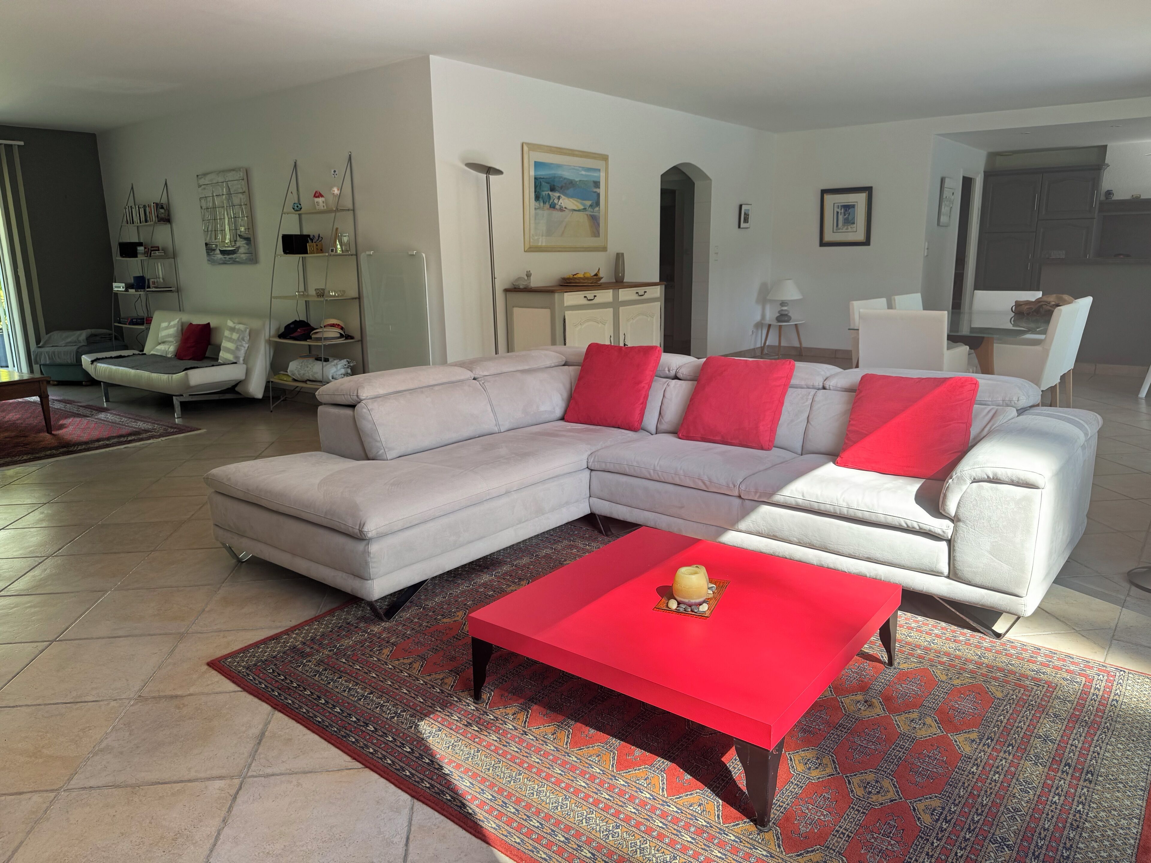 Un salon moderne avec un canapé d’angle, une table basse rouge et un tapis à motifs.