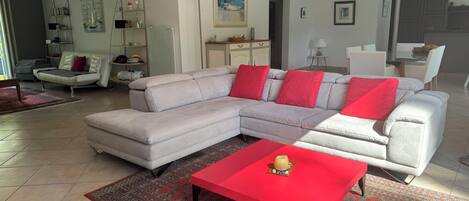 Ein modernes Wohnzimmer mit einem Ecksofa, einem roten Couchtisch und einem gemusterten Teppich.