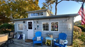Ein kleines Haus mit Veranda, zwei blaue Adirondack-Stühle, ein kleiner Tisch und eine Flagge.