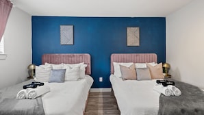 Ein Doppelzimmer mit zwei Betten, jeweils mit rosa Kopfteil, weißer Bettwäsche und einem kleinen Nachttisch mit Lampe.