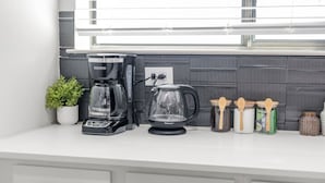 Eine Küchenarbeitsfläche mit Kaffeemaschine, einem Glasbehälter und verschiedenen Küchenutensilien.