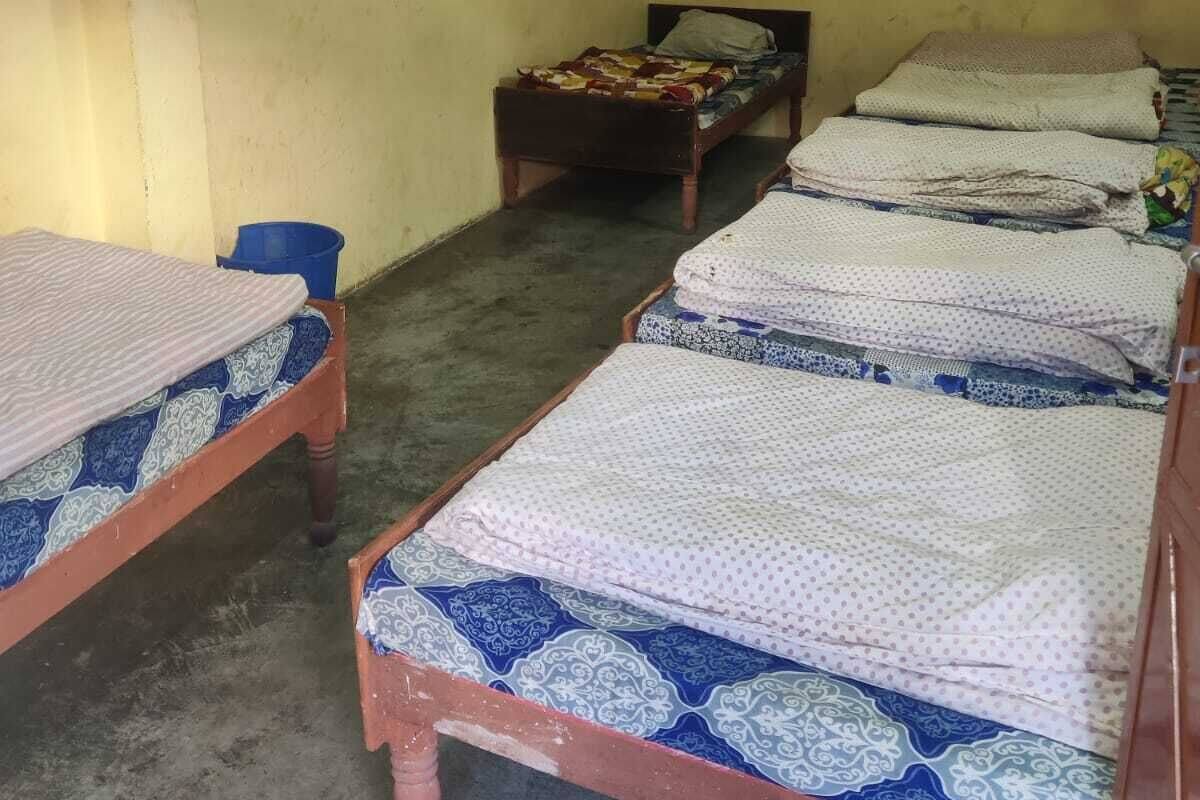 A dormitory room with four single beds, a blue bucket, and a ceiling fan.