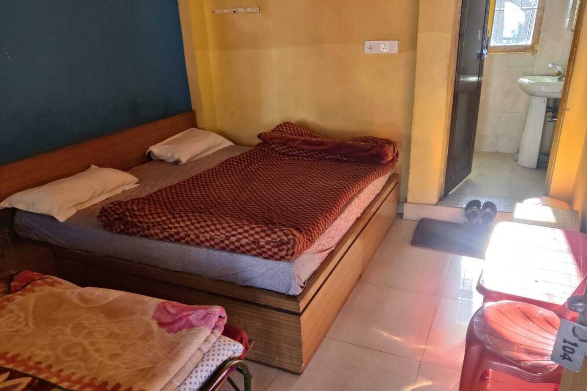 A small, single-bed room with a wooden headboard, a checkered blanket, and a pair of slippers on the floor.