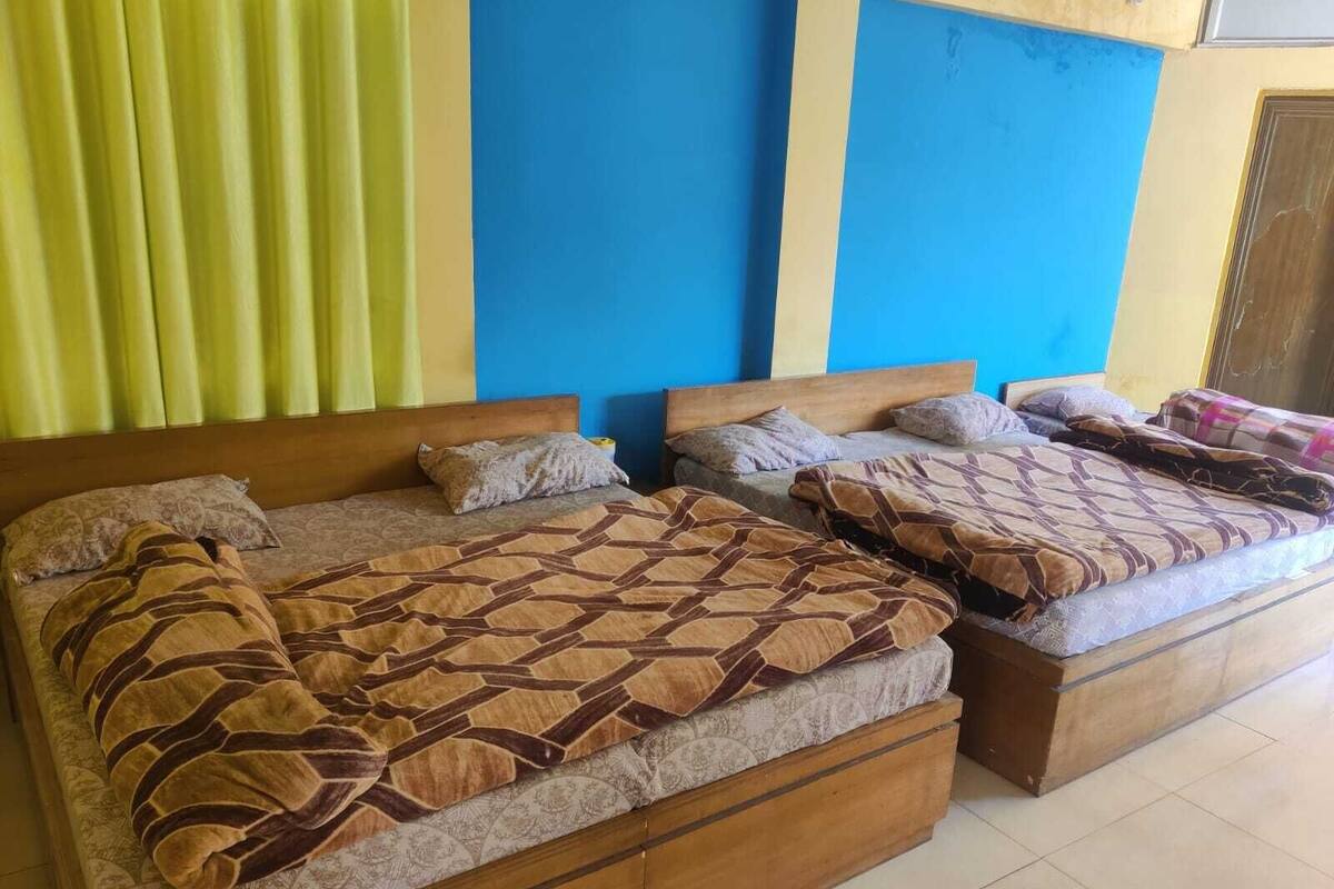A hotel room with three beds, each with a wooden headboard and multiple pillows. The room has a tiled floor and a window with yellow curtains.