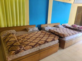Habitación de hotel con tres camas, cada una con cabecero de madera y múltiples almohadas. La habitación tiene piso de baldosas y una ventana con cortinas amarillas.