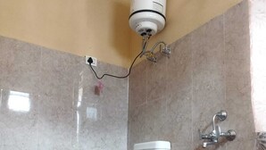 Un baño con inodoro, un cubo rojo y un calentador de agua instalado en la pared.