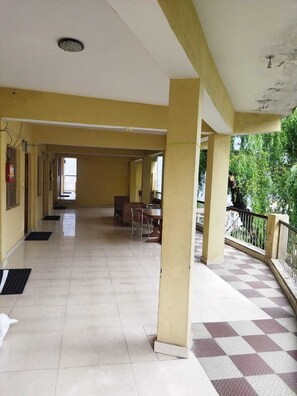 A spacious corridor with tiled flooring, a checkered outdoor area, and a view of greenery outside. - Jain Rest House (Joshimath)