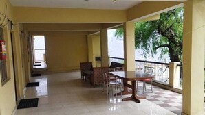 Un espacio interior amplio con suelo de baldosas, una mesa de comedor con sillas y vistas a un árbol fuera.