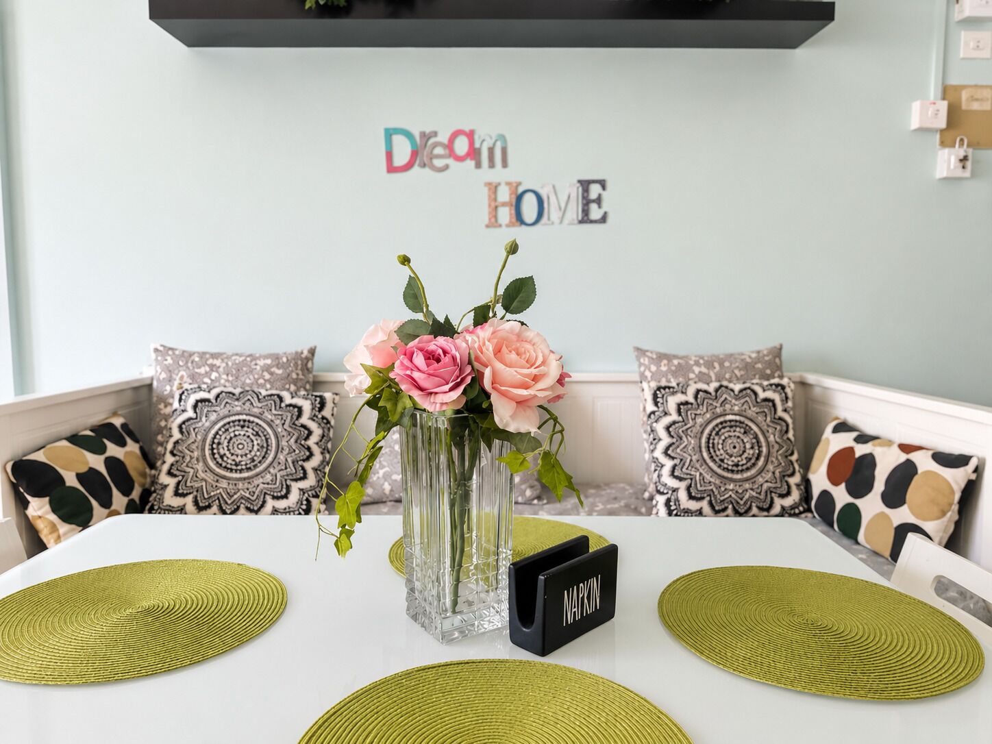 A dining table with a vase of flowers, placemats, and a napkin holder labeled 'NAPKIN'.