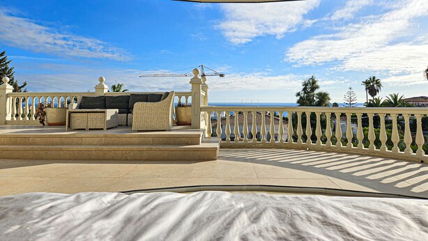 Un balcon spacieux avec vue sur la mer, un coin salon agrémenté de coussins et une balustrade décorative.