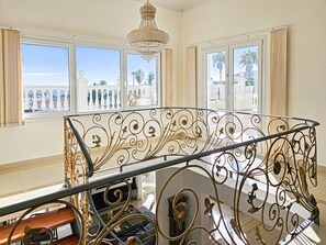 A spacious balcony with ornate metal railings and a chandelier, overlooking a coastal area with palm trees. - Villa with private pool and hot tub Mijas Costa (Mijas Costa)