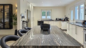 Une cuisine moderne dotée d’un grand îlot en granit, d’appareils électroménagers en acier inoxydable et bénéficiant d’un éclairage naturel abondant grâce à de grandes fenêtres.