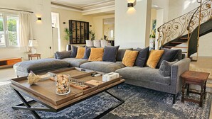 Un salon moderne avec un canapé d’angle, une table basse et un escalier doté de rampes décoratives.