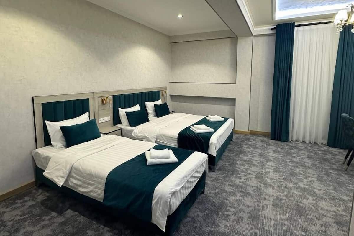 Ein Hotelzimmer mit zwei Betten, einem großen Fenster mit Vorhängen, einer Deckenlampe und einem Teppichboden.