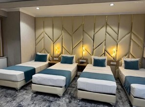 A hotel room with four beds arranged in a row, each with a nightstand and lamp. The room has a modern design with a geometric wall pattern and a marble floor. - BlueShore International hotel (Tashkent)
