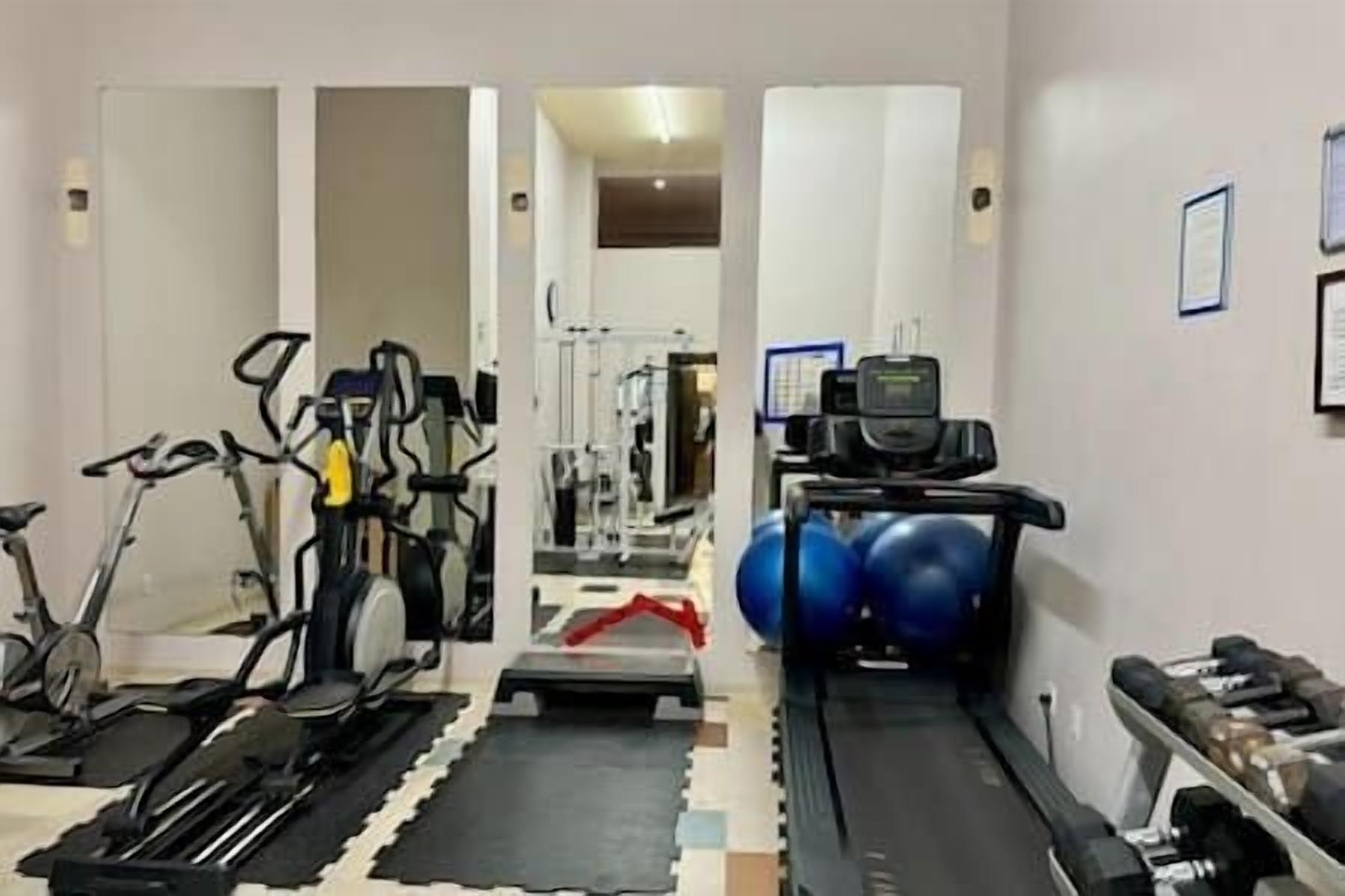 Ein Fitnessraum mit Trainingsgeräten, Laufband und Gewichthecke.