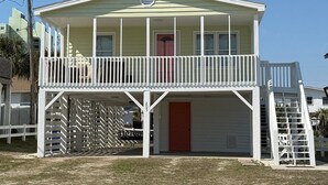A two-story building with a balcony, a red door, and a white fence. - Cute Bungalow in Cherry Grove, SC. Just a Chip Shot from ocean & beach access! (North Myrtle Beach)